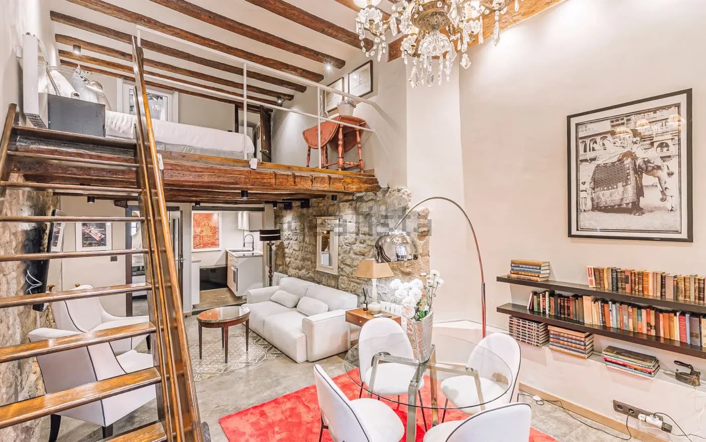 Vista general del loft con el altillo, la cama sobre la viga y la librería
