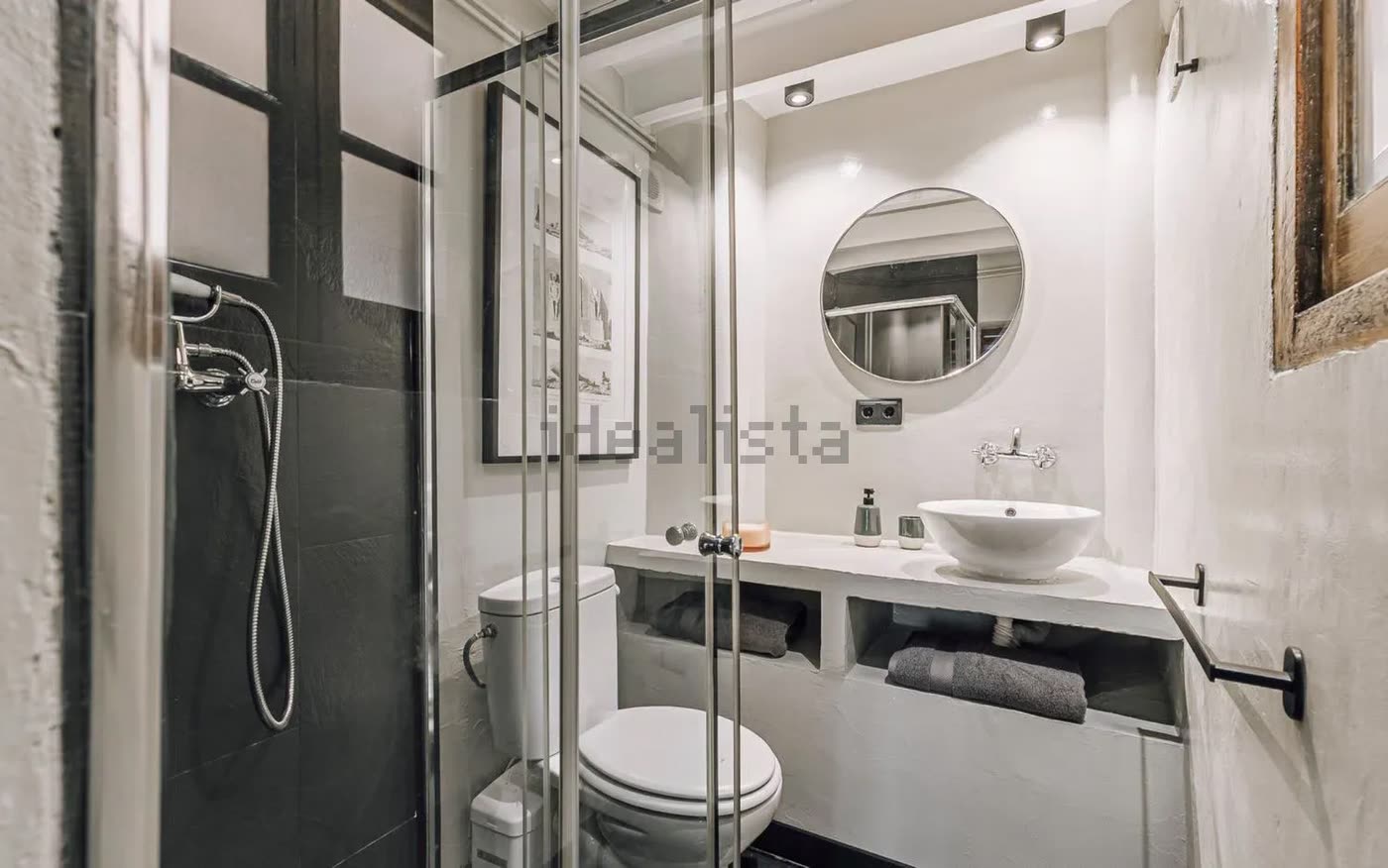 Baño reformado con ducha, espejo redondo y lavabo sobre encimera de obra