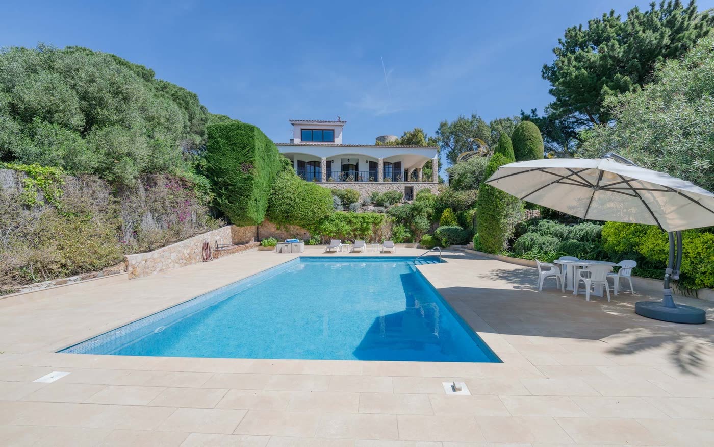 Piscina de la masía con la casa de piedra al fondo y sombrilla junto al agua